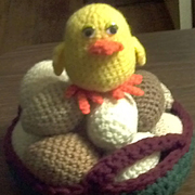 This cute baby chick sits on a pile of crocheted eggs.